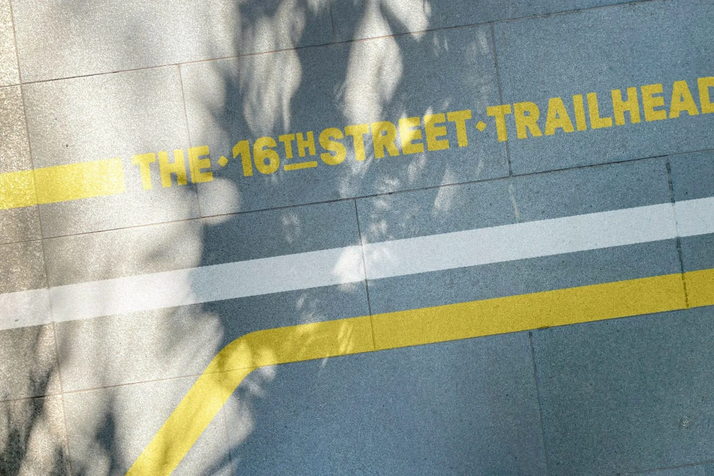 보도를 가로지르는 노란 선과 THE 16TH STREET TRAILHEAD 각인